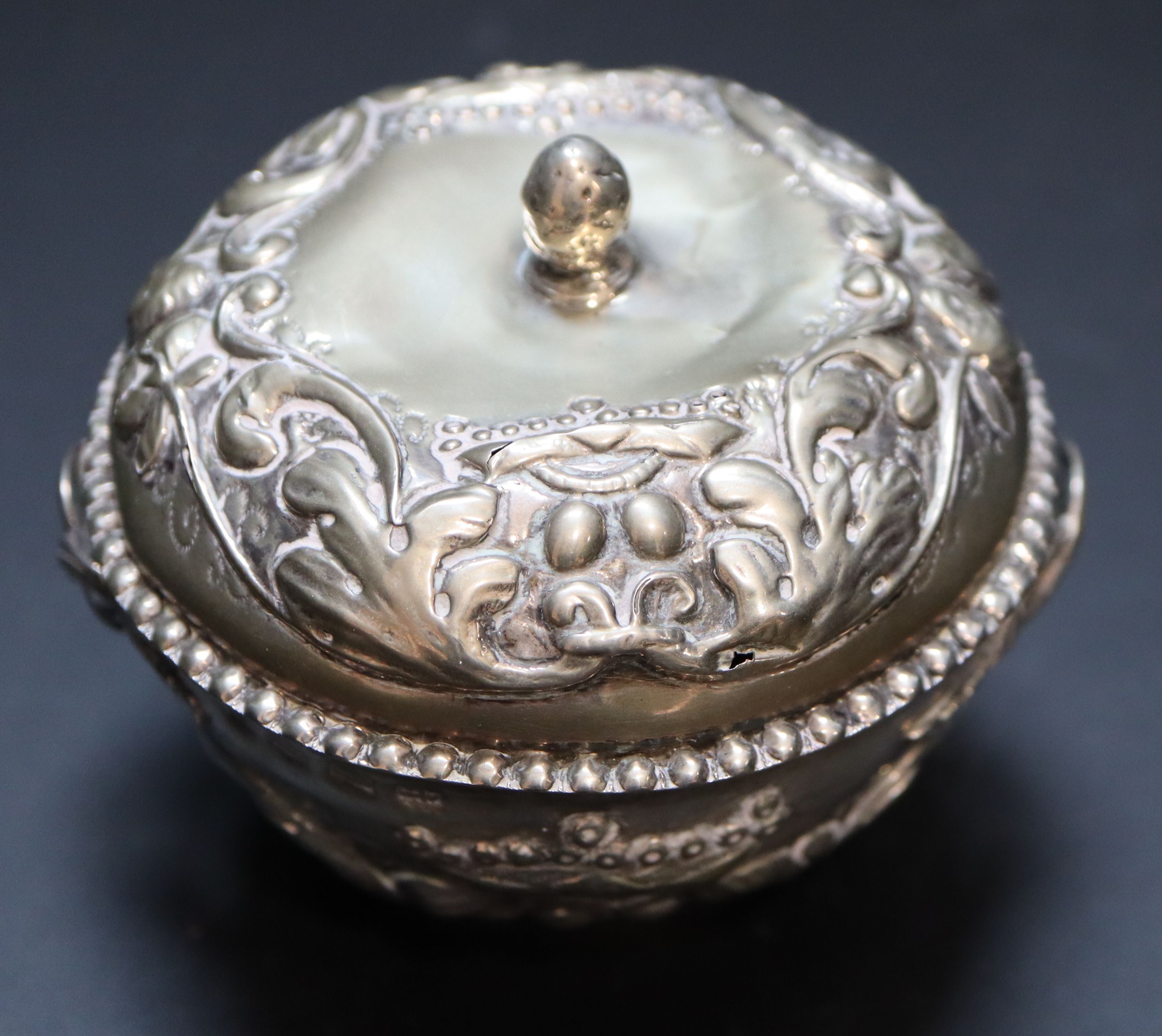 A 19th century Continental circular embossed white metal two handled pot and cover, 83mm, 99 grams. (a.f.)